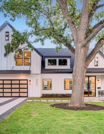 Modern two-story house with a large front yard tree and a double garage at dusk.