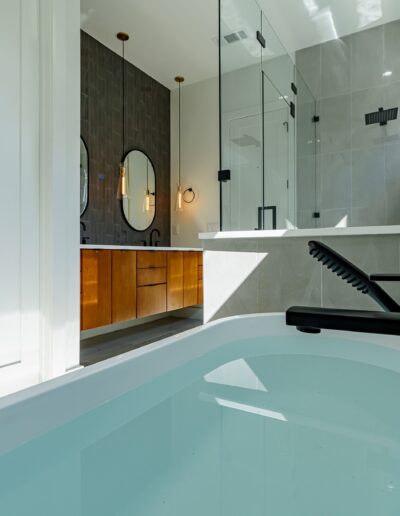 Modern bathroom interior featuring a bathtub, glass shower stall, double vanity with round mirrors, and gray tiles.