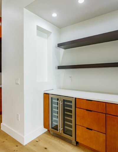 Modern kitchen corner with wooden cabinets, stainless steel appliances, and floating shelves.