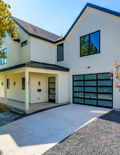 Modern two-story house with white exterior, black trim, and attached garage, surrounded by landscaped yard.