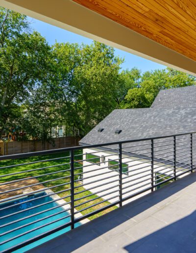 Spacious balcony with a metal railing overlooking a backyard with a swimming pool and greenery on a bright sunny day.