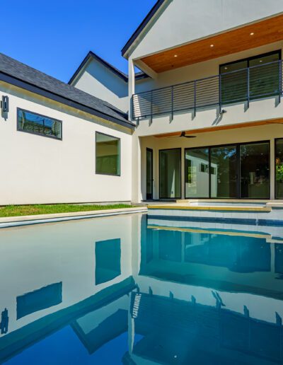 Modern backyard with a swimming pool and a contemporary two-story house with large windows and a balcony.