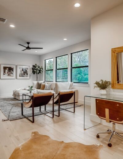 Modern home office with a minimalist design, featuring a wooden desk, ergonomic chair, and a cozy sitting area near large windows.