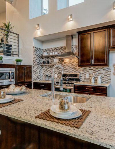 A modern kitchen interior with dark cabinets, stainless steel appliances, a tiled backsplash, and a center island with a sink.