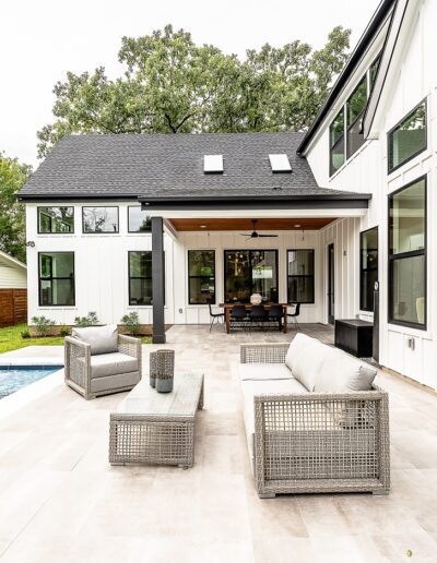 Modern backyard with a swimming pool, patio seating, and a covered outdoor dining area adjacent to a house with large windows.