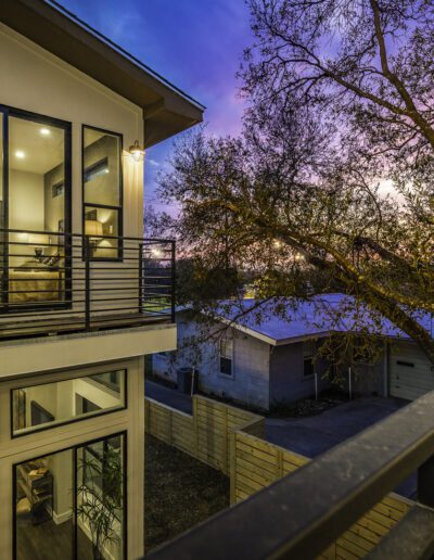 Modern house with large windows during twilight, showcasing interior lights and a view of trees under a colorful sky.