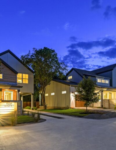 Two-story houses illuminated by exterior lights at twilight.