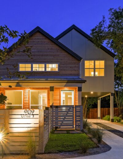 Modern two-story house illuminated at twilight with a wooden fence and landscaped walkway.