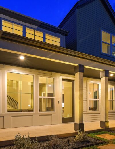 Modern two-story home illuminated at dusk with a well-lit porch and accent lighting.